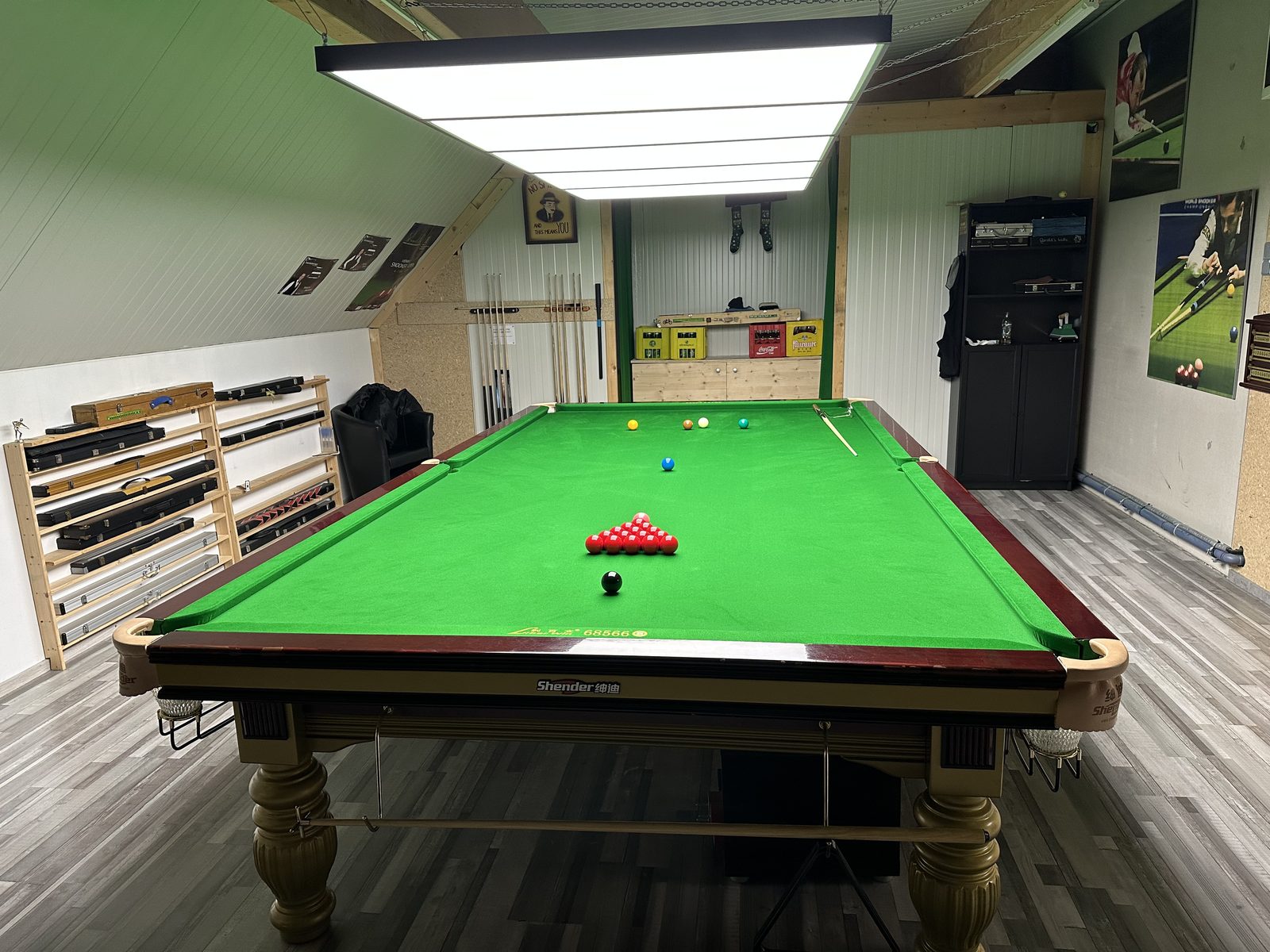 Ein spielbereiter Snookertisch, an der Wand das Queue-Regal
